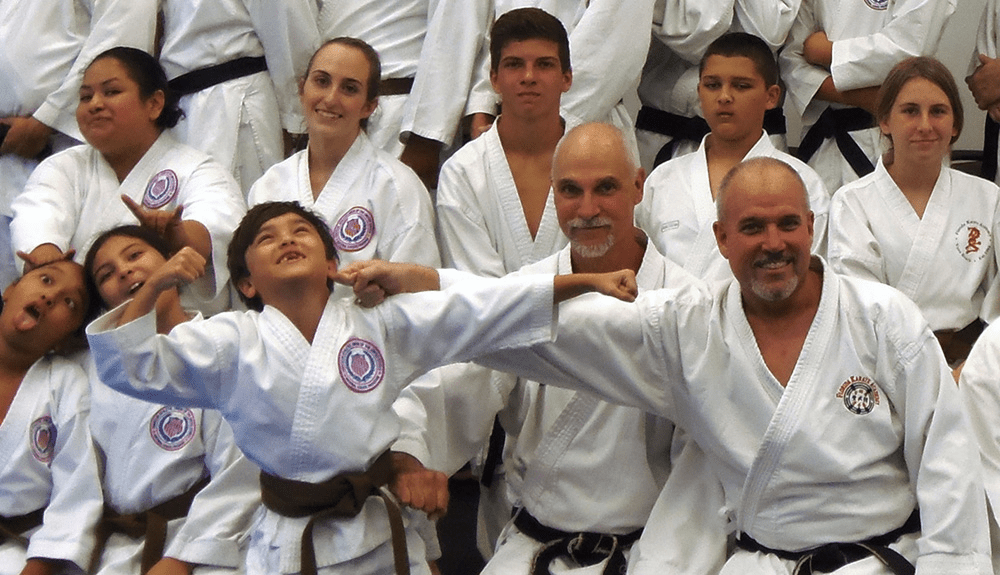 Karate class group posing; a child playfully flexes while an instructor holds his arm.