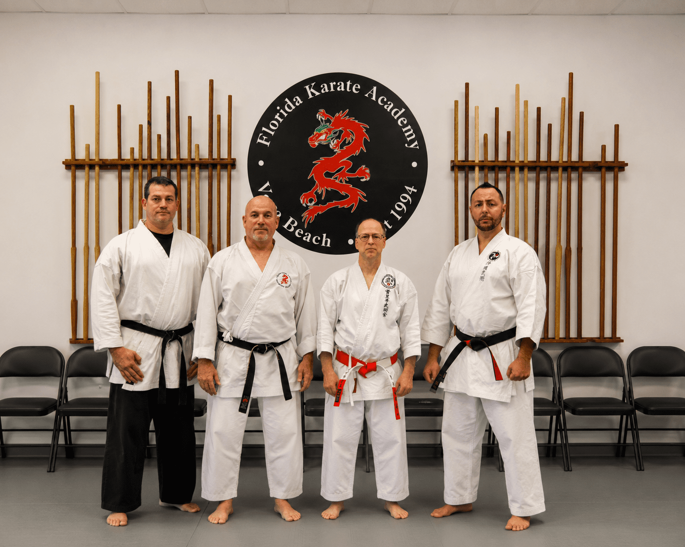 Four adult martial artists standing under academy logo