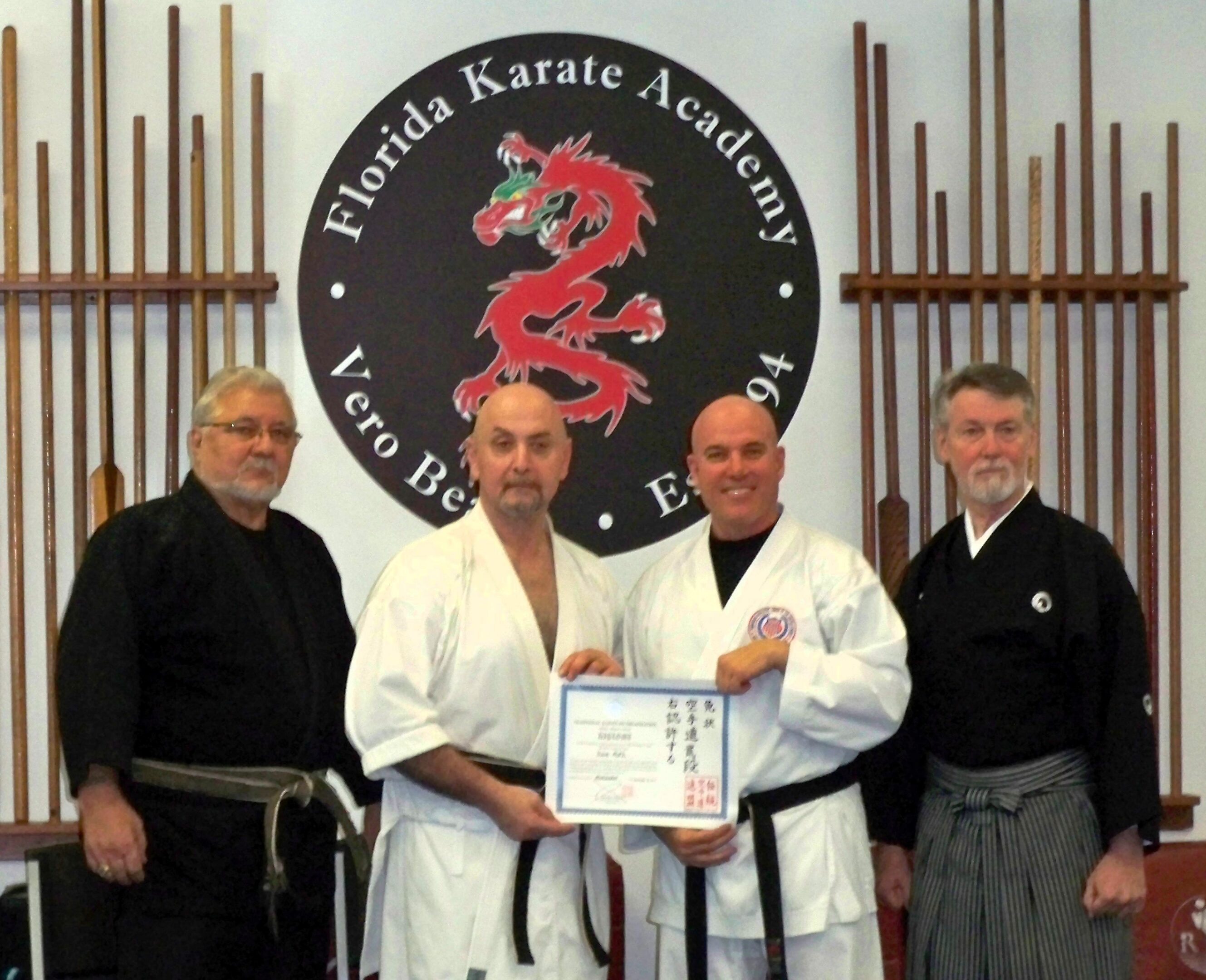 Four dojo instructors standing before dragon emblem