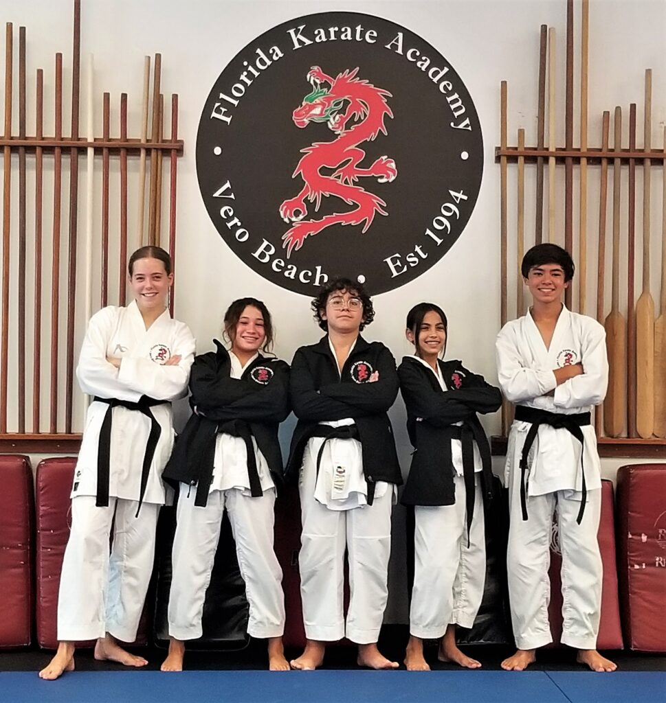 Florida Karate Academy students posing together in karate uniforms in front of the academy logo.